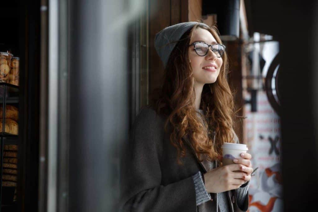 Happy attractive young woman thinking and drinking coffee outdoors