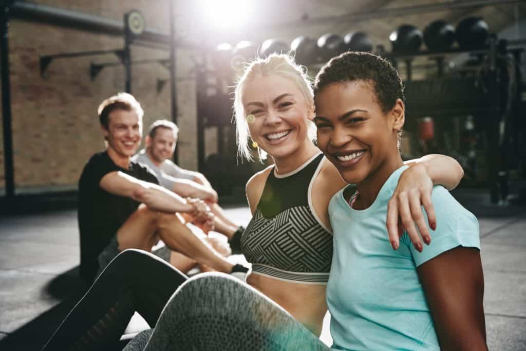 Two laughing women sitting in a gym after working out