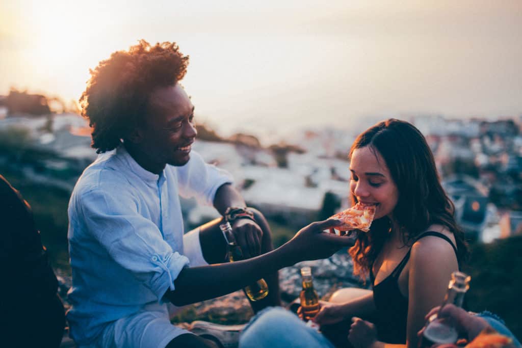Couple enjoying pizza and beer under a sunset