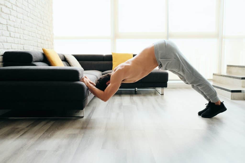 Man Training Chest And Triceps Doing Skull Crunches Using Sofa